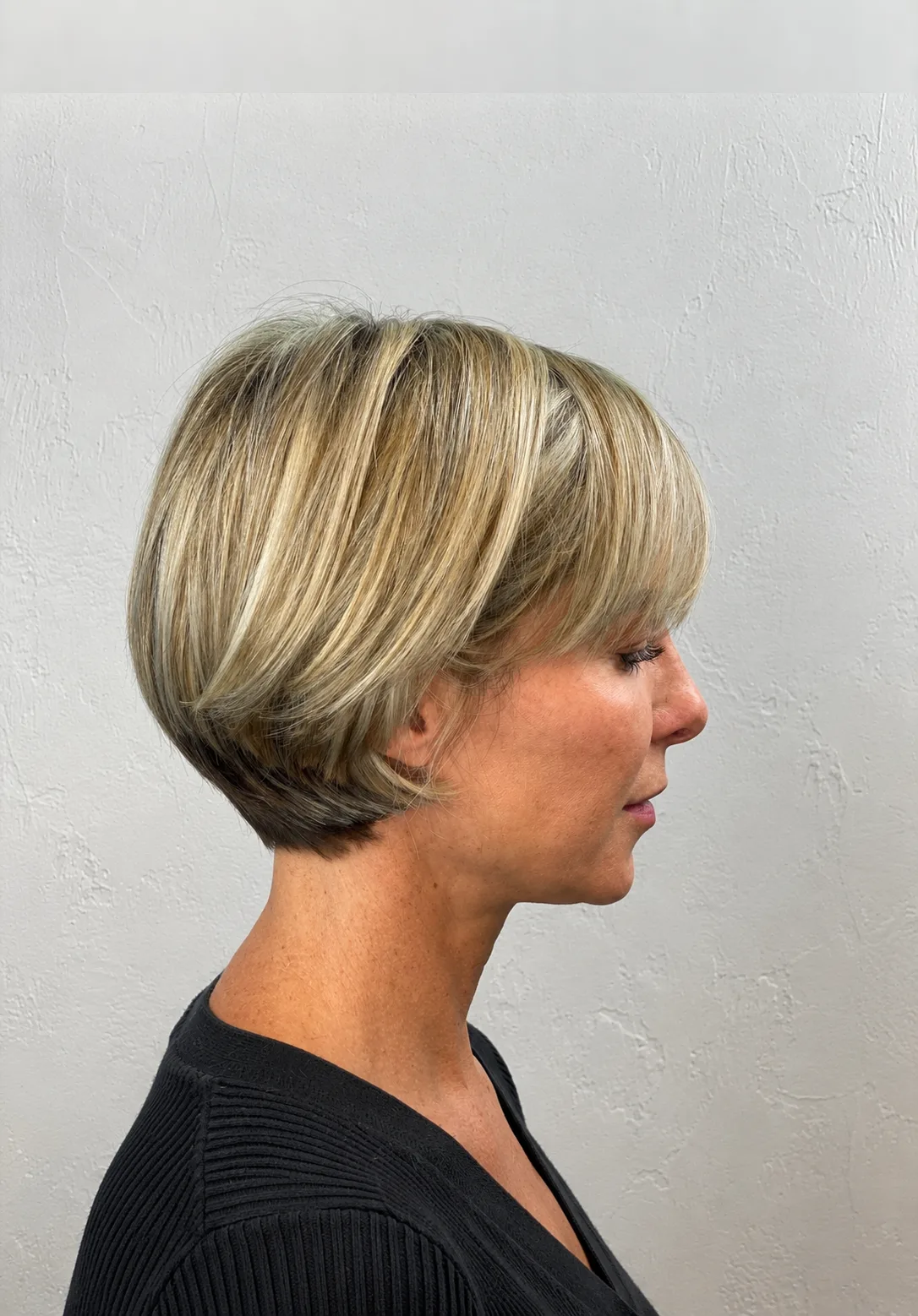 Jaw-length rounded blonde bob with a soft fringe and highlights, side profile